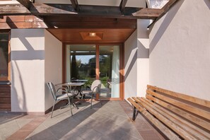 An outdoor patio with a table and chairs, a wooden bench, and a glass door leading to a garden. - Apartment at Hotel and Residences Theresia with Mountain View and Private Terrace (St. Leonhard in Passeier)