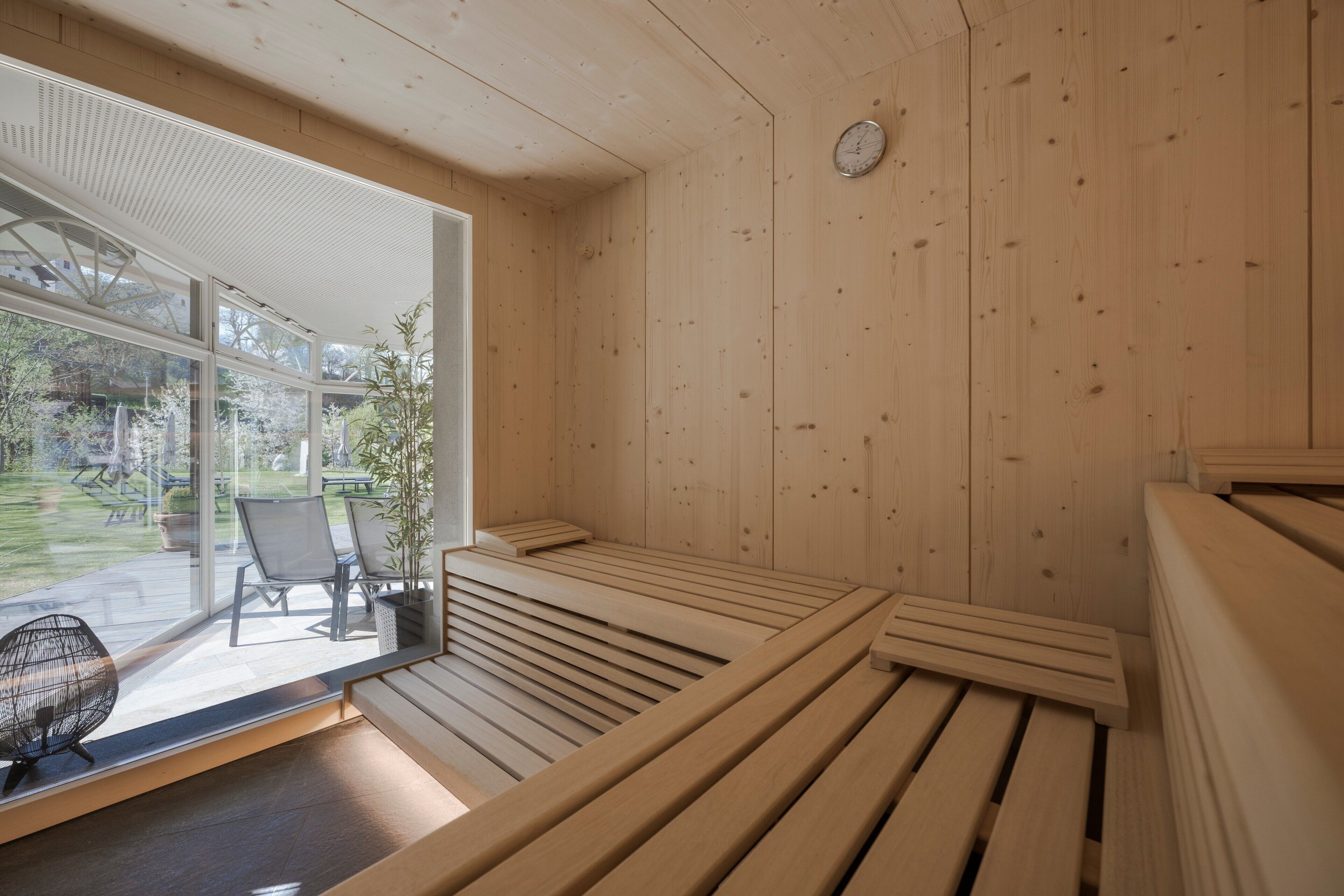 A wooden sauna with benches and a glass door leading to an outdoor area with chairs and a table.