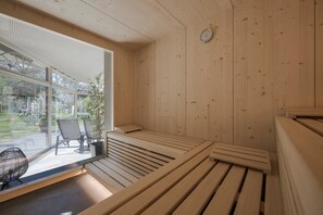 Una sauna de madera con bancos y una puerta de cristal que da a un espacio exterior con sillas y una mesa.