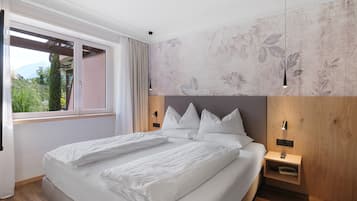 A modern bedroom with a large bed, a wooden headboard, and a view of greenery outside.