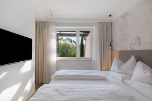 Un dormitorio con cama, sofá, televisor y ventana con cortinas.