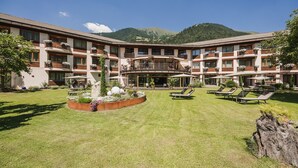 Un hotel de varios pisos con patio central, mobiliario exterior y vistas a la montaña.