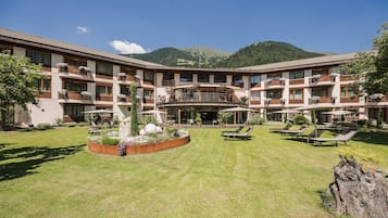 Ein mehrstöckiges Hotel mit Innenhof, Außenbestuhlung und Bergblick.
