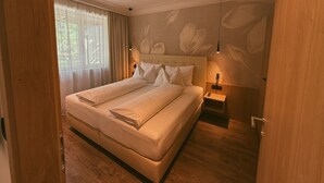 Una cama doble con cabecera, mesitas de noche y una ventana con cortinas.