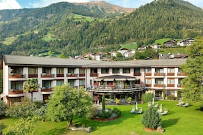 Un hotel con numerosi balconi, un cortile interno con posti a sedere all'aperto e montagne sullo sfondo.