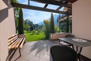 A patio with a wooden bench, a table, and chairs, overlooking a well-maintained lawn and distant mountains. - Apartment at Hotel and Residences Theresia with Mountain View and Private Terrace (St. Leonhard in Passeier)