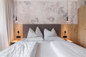 Ein Doppelbett mit Holz-Kopfteil, zwei Nachttische mit Lampen und eine Wand mit Blumenmuster.
