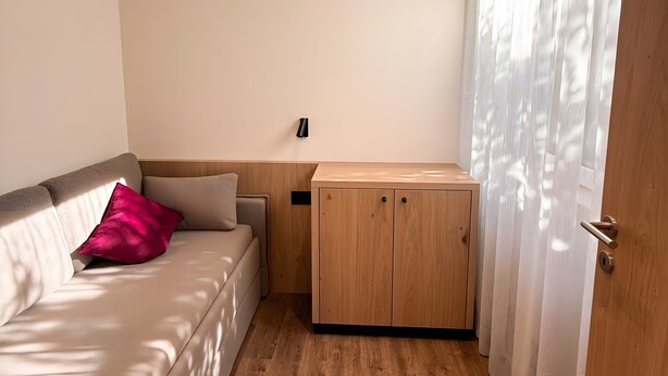 Una habitación con un sofá, un armario de madera y una puerta con cortinas.