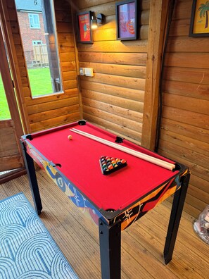 A pool table with a red felt surface, surrounded by wooden walls with framed artwork. - Bright Contemporary Home, Games Room & Exceptional Outdoor Entertaining Areas (Saltney)