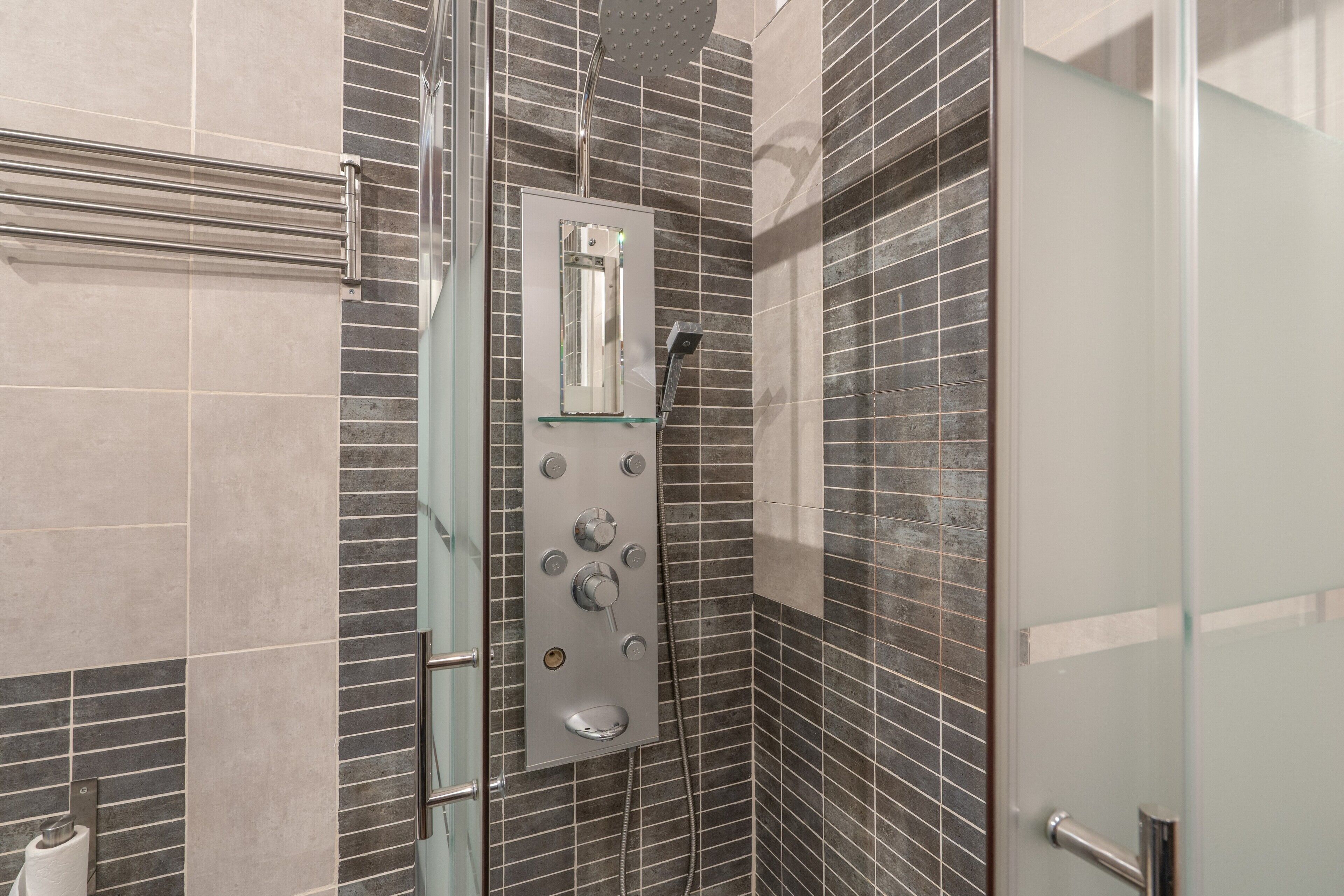 Un baño moderno con cabina de ducha de vidrio, ducha de mano y panel de control en la pared.