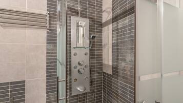 Un baño moderno con cabina de ducha de vidrio, ducha de mano y panel de control en la pared.