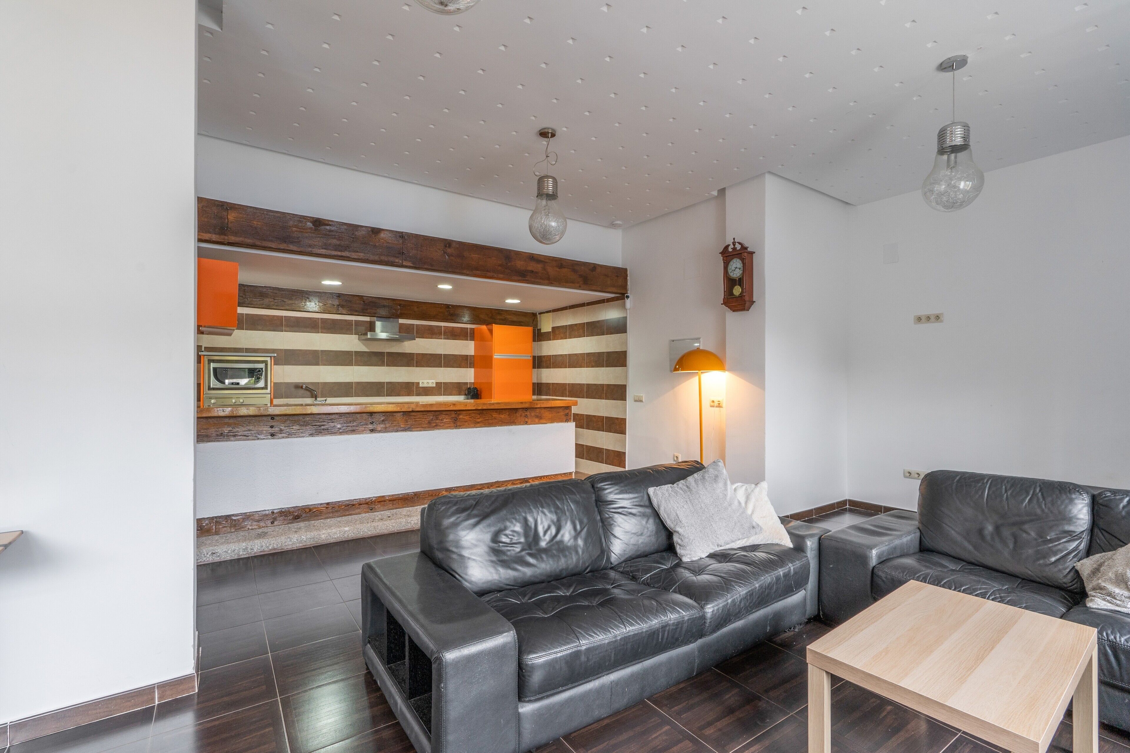 Ein modernes Wohnzimmer mit einer Ledersofa, einem Holztisch und einer Küchenzeile mit eingebautem Ofen und einer Holzrückwand.