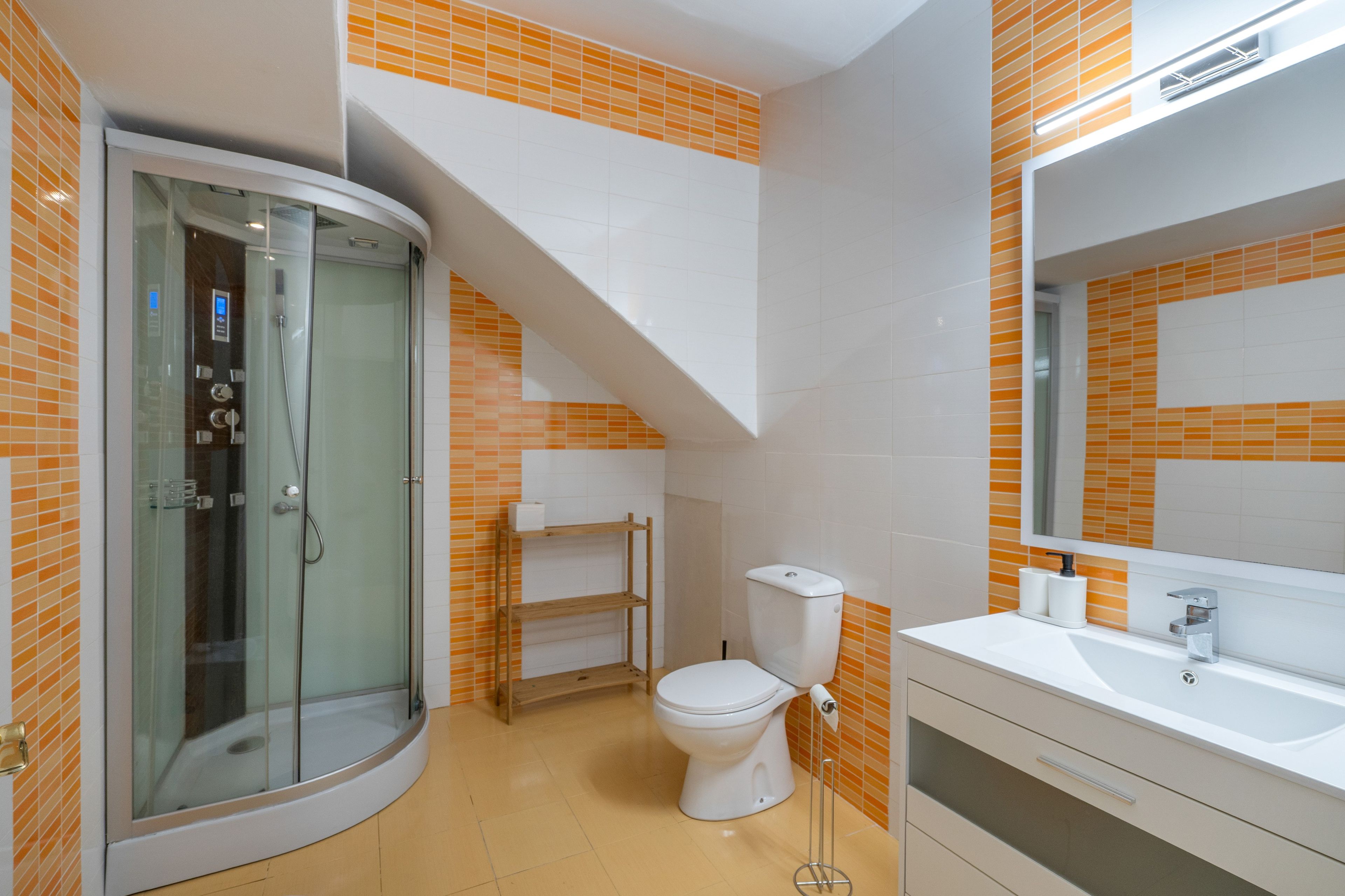 Un baño moderno con cabina de ducha de vidrio, inodoro y lavamanos con espejo.