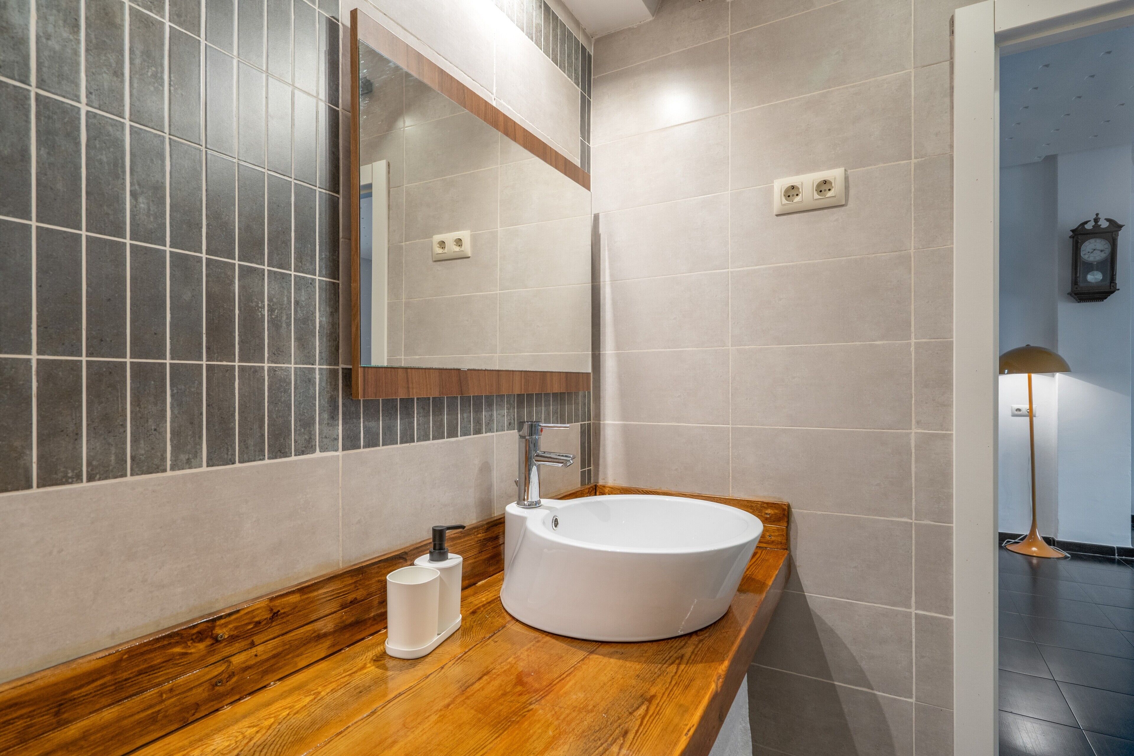 A bathroom with a wooden vanity, a white sink, and a mirror.
