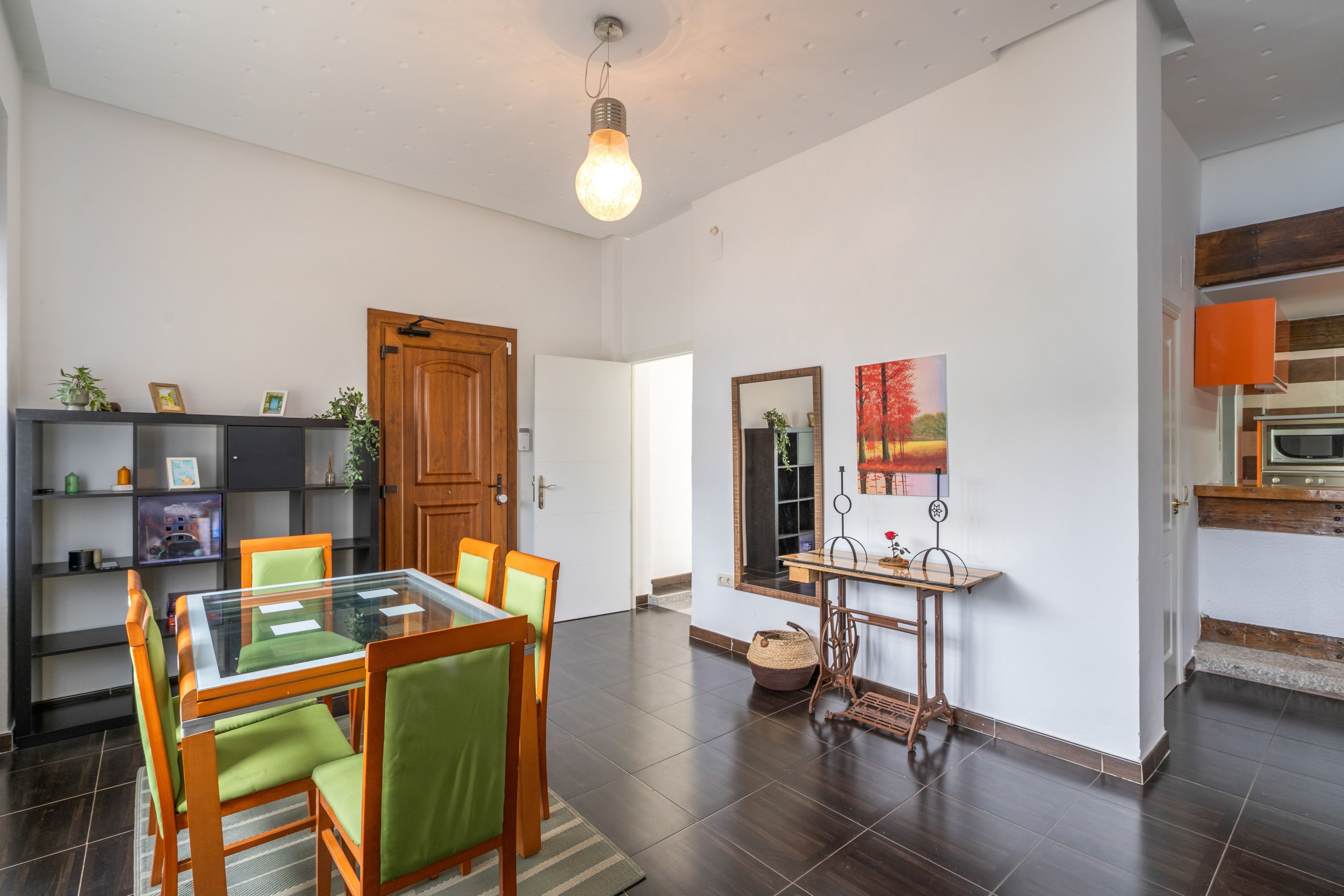 Un comedor moderno con una mesa de vidrio y sillas de madera, una puerta de madera, y una cocina con microondas.