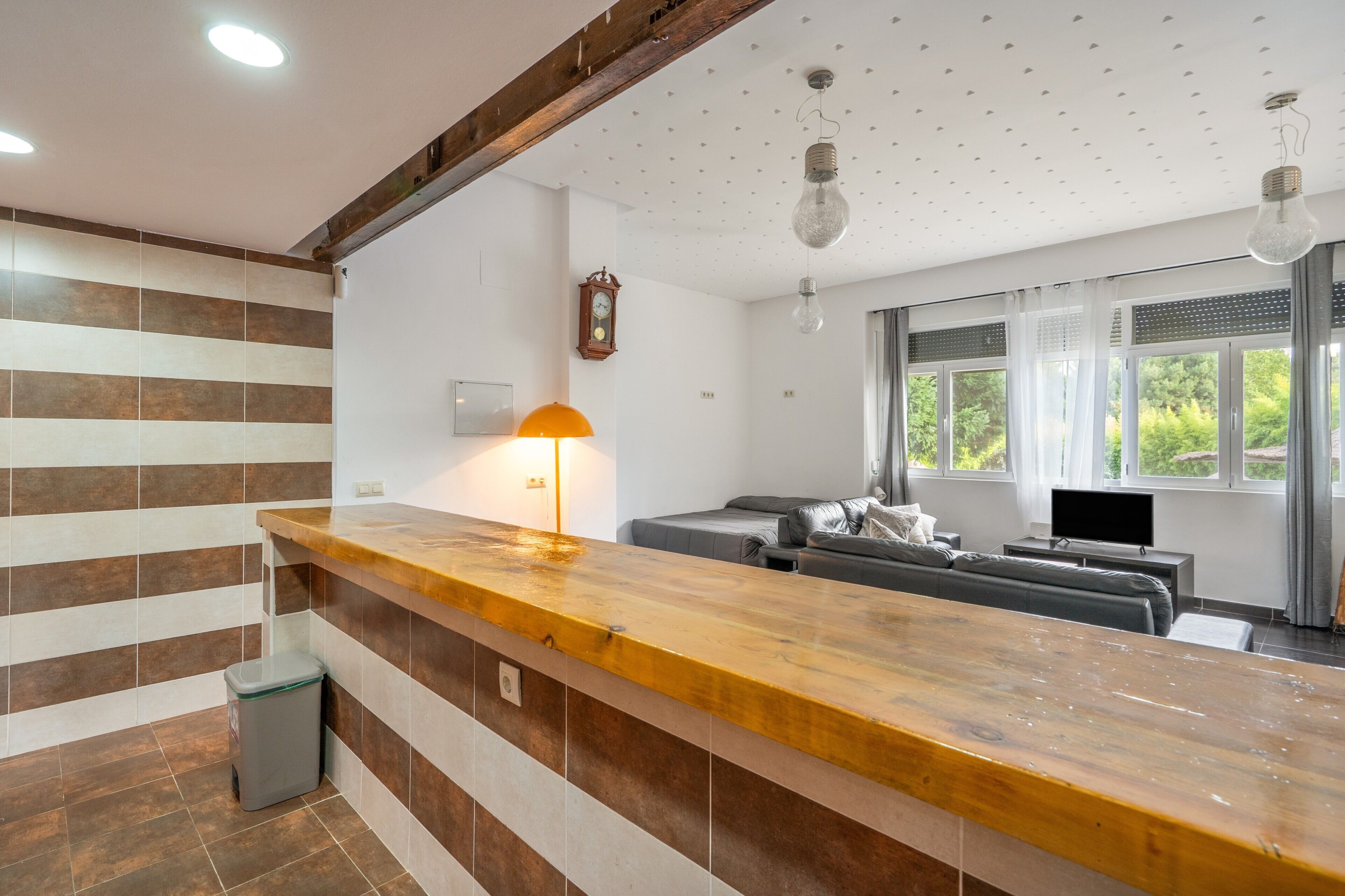 Una cocina moderna con encimera de madera, un contenedor de basura empotrado y un comedor con sofá y televisor.
