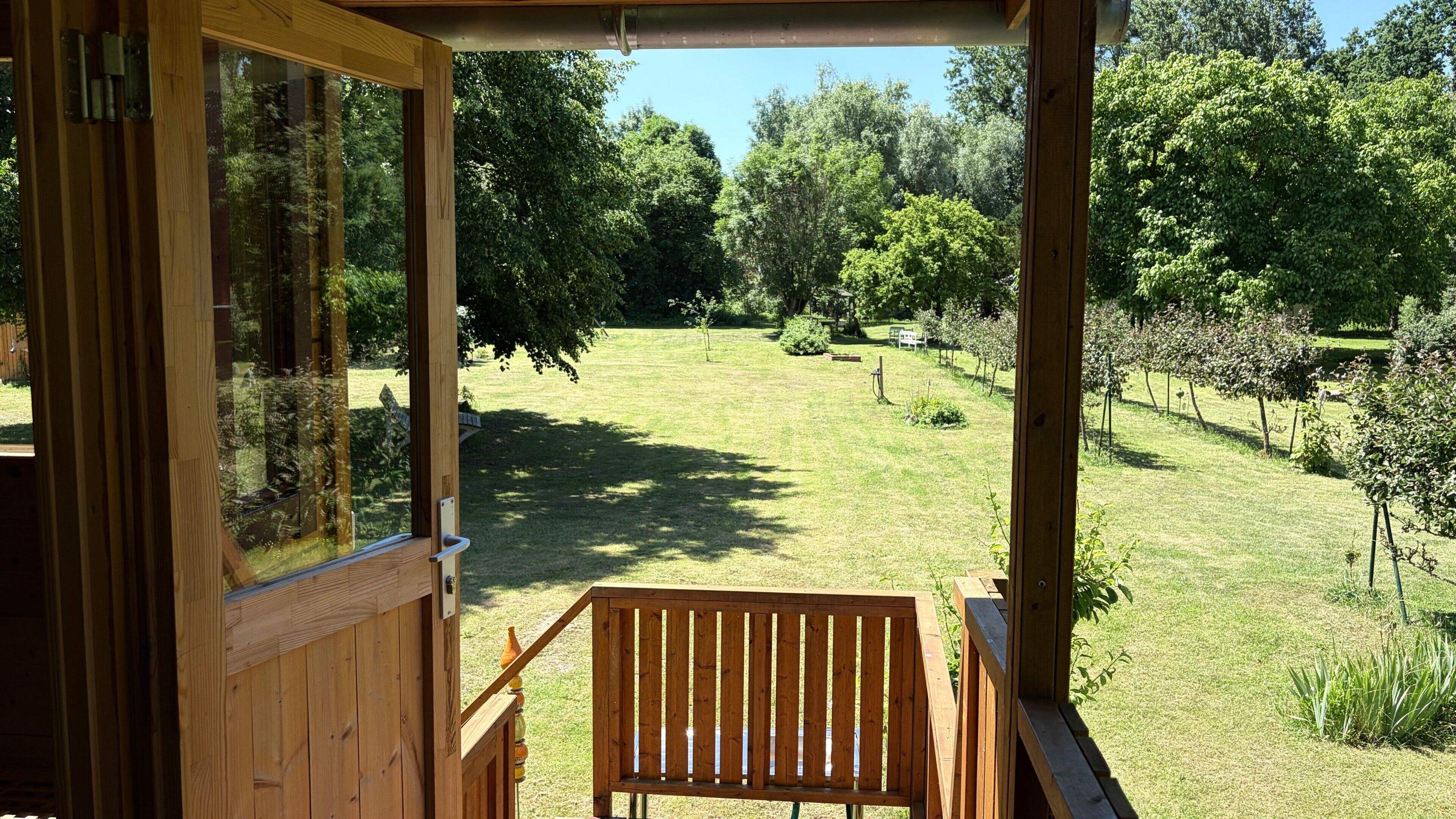 Eine Holzterrasse mit einer Bank, mit Blick auf einen Rasen mit Bäumen und einem klaren Himmel.