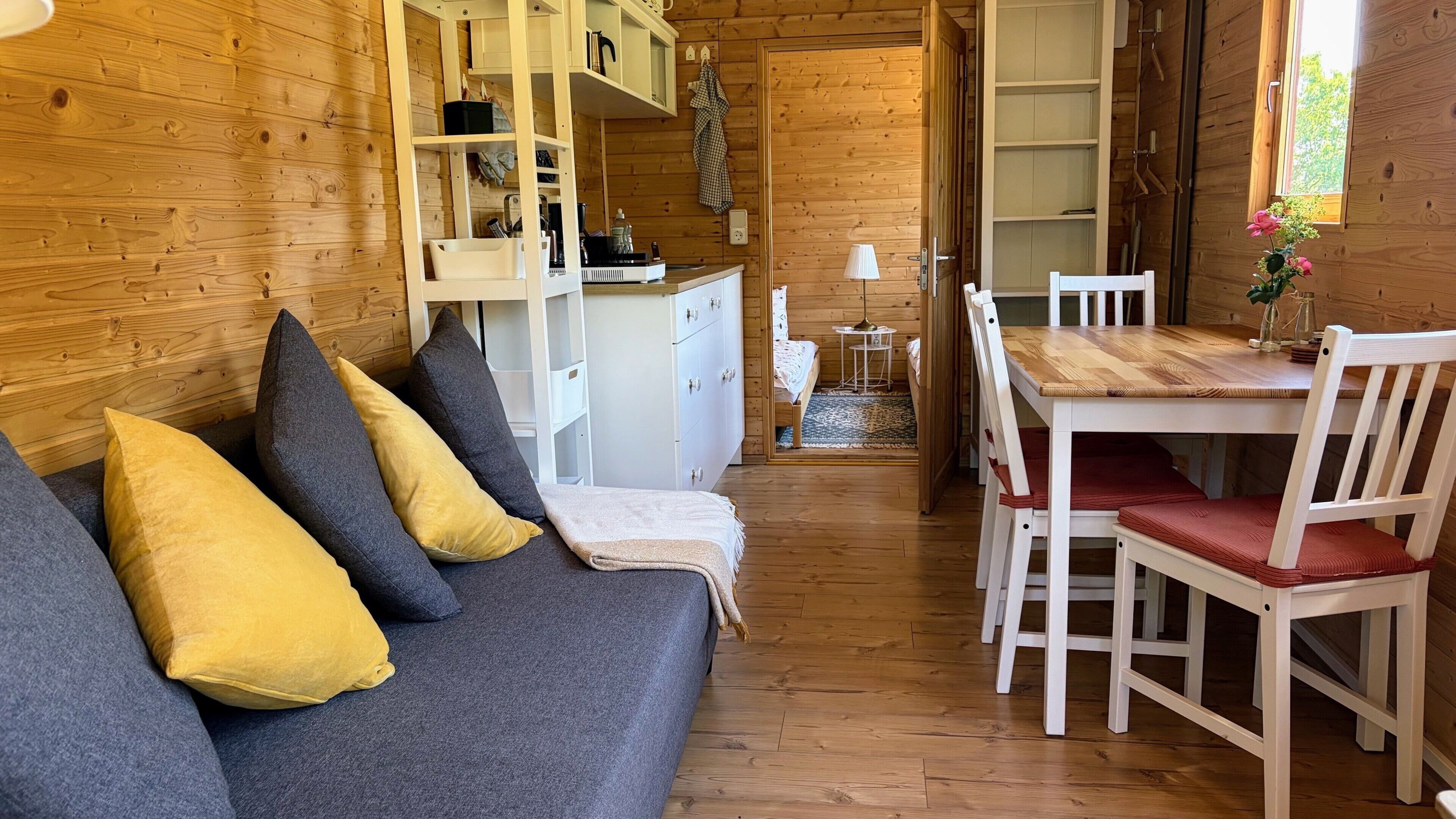 Ein gemütliches Blockhaushaus-Interieur mit einer Couch, einem Esstisch, Stühlen und einer Küchenzeile.