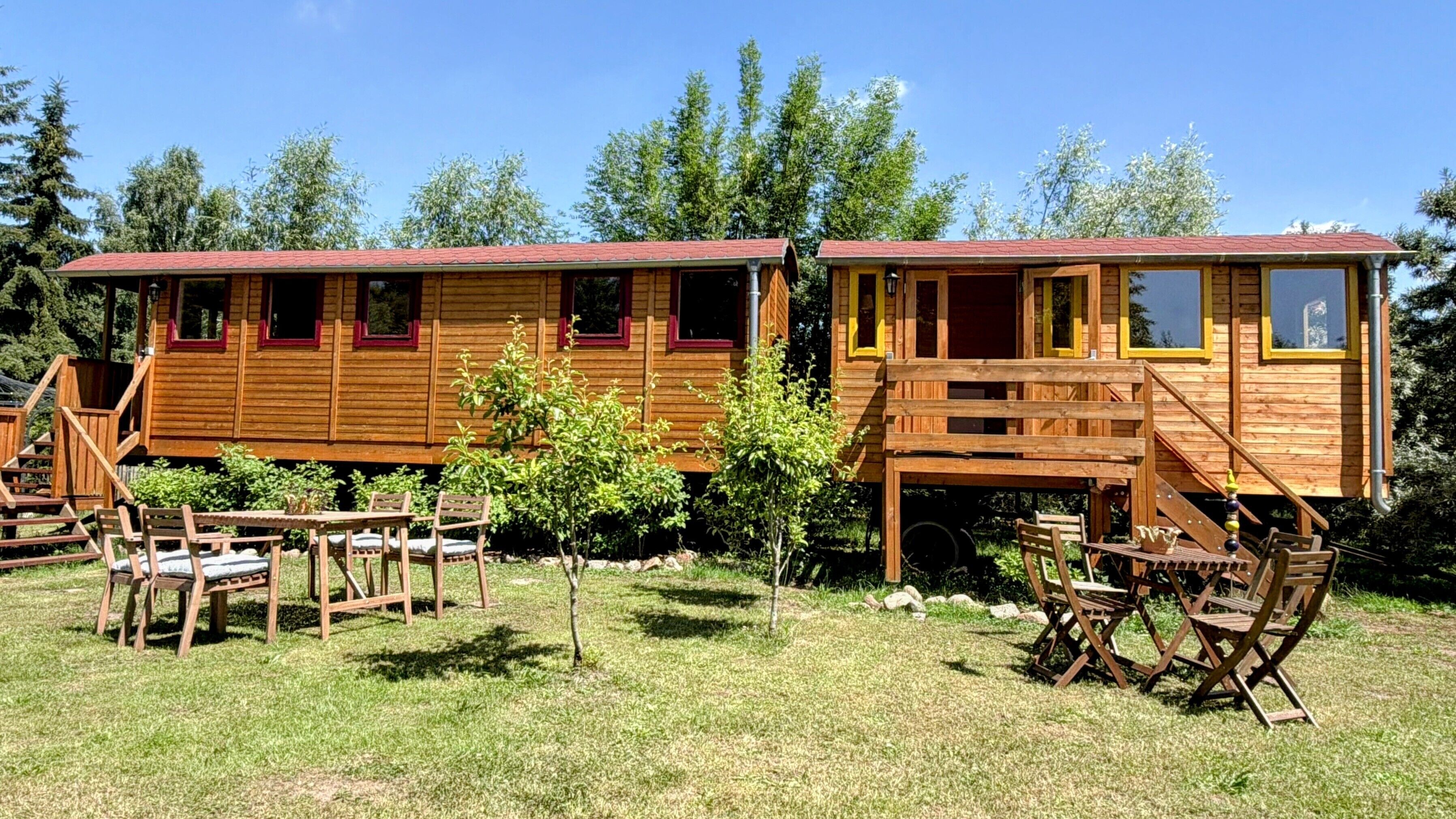 Dos cabañas de madera con escaleras exteriores, una mesa de picnic y sillas en un área con césped.