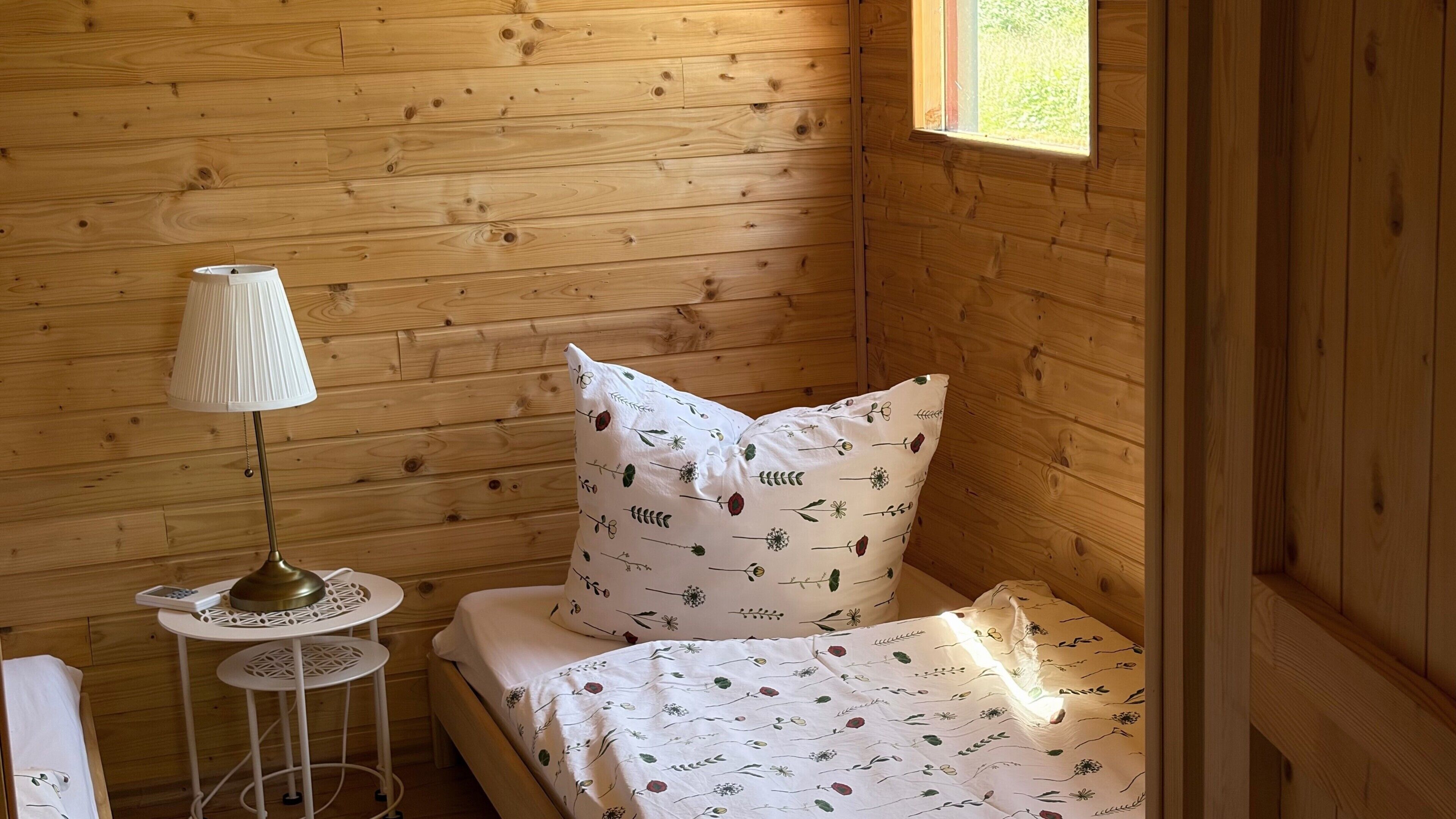 A wooden cabin room with a bed, a lamp, and a small table.
