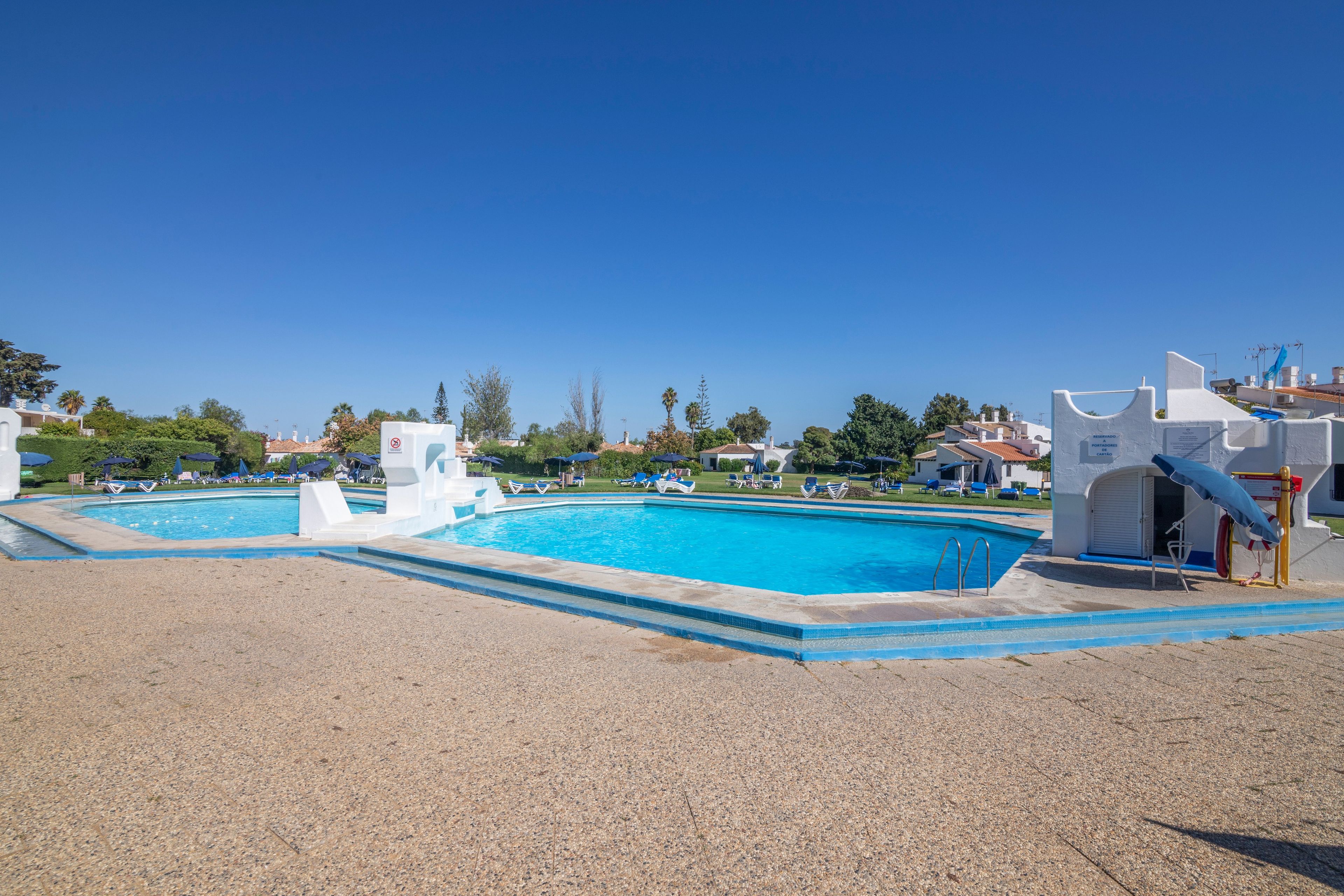 A swimming pool with a white structure, surrounded by lounge chairs and umbrellas.