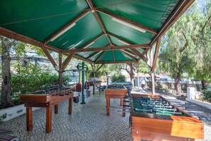 An outdoor recreational area with multiple foosball tables and a covered seating area. - Holiday Home 'Apartamento Nascimento' with Shared Pool, Private Terrace and Air Conditioning (Santa Luzia)