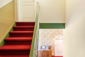 A staircase with red carpeted steps leading to a landing with a wooden desk, a wall with floral wallpaper, and a door. - Apartment 'Haus Kuhlmann Mit Schlafsofa' with Mountain View, Shared Garden and Wi-Fi (Landkreis Goslar)