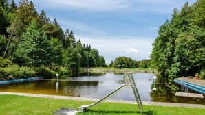 Um parque com um lago, um escorrega de metal e um deck de madeira.