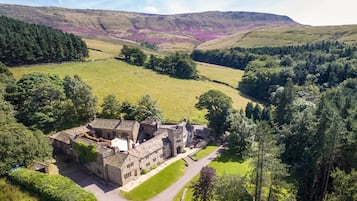 A stone building with multiple rooms and a courtyard, surrounded by lush greenery and hills.