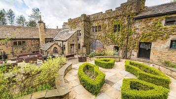 A courtyard with stone buildings, a central seating area, and neatly trimmed hedges.