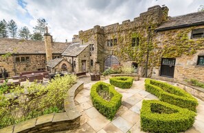 Un patio con edificios de piedra, una zona de estar central y setos podados.
