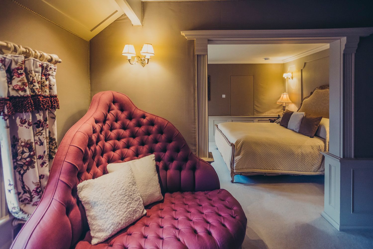 Un dormitorio con una cama grande, un sillón tapizado en rojo y un espejo que refleja la habitación.