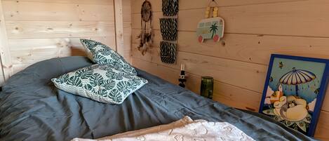 A wooden room with a bed, pillows, a dreamcatcher, a wall hanging, and a framed picture.