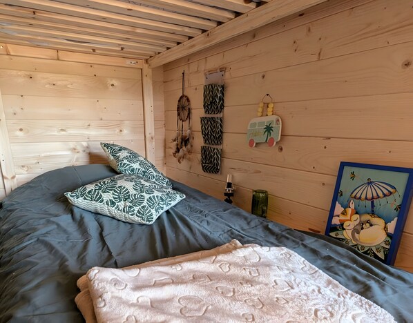 Een houten kamer met een bed, kussens, een dromenvanger, een wanddecoratie en een ingelijst schilderij.