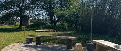 Un espacio al aire libre con una chimenea de piedra, bancos de madera y una mesa de picnic.