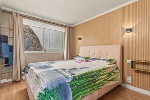 A bedroom with a bed, a window, wooden panel walls, and a wall-mounted light fixture.