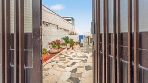 Une ruelle étroite, dallée, qui mène à un bâtiment dont le mur est blanc et qui offre une vue sur la mer.
