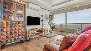 Ein modernes Wohnzimmer mit einem Ledersofa, einem Fernseher und einer Holzkassette mit geometrischen Mustern.