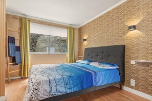 A bedroom with a bed, a window, a wall-mounted light, and a towel rack.