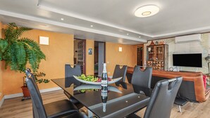 Un coin repas moderne avec une table en verre, des chaises noires, un saladier rempli de fruits et une bouteille de vin.