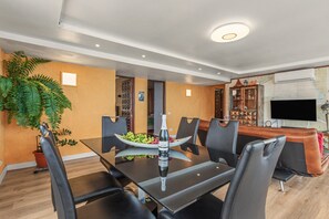 A modern dining area with a glass table, black chairs, a bowl of fruit, and a bottle of wine.