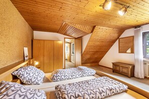 A bedroom with a sloped ceiling, wooden walls, a bed with patterned bedding, a bedside table, and a mirror. - Apartment 'Fewo Wrede Am Sauerland-Radring 2' with Mountain View, Balcony and Wi-Fi (Eslohe)