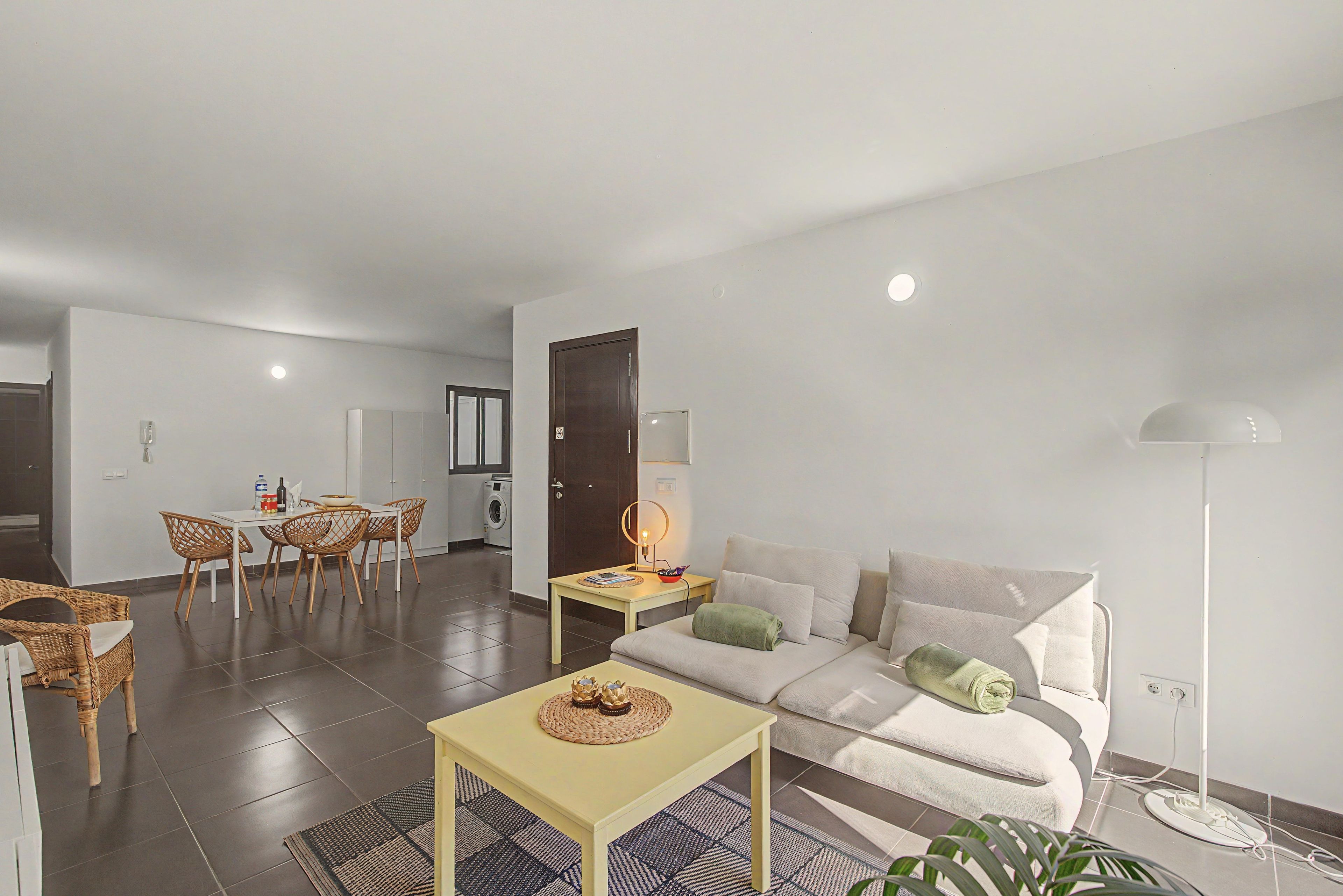 A modern living room with a sofa, a dining table with chairs, a lamp, and a floor lamp.