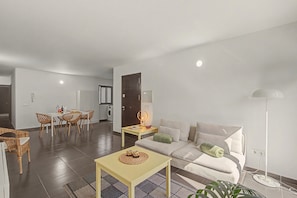 A modern living room with a sofa, a dining table with chairs, a lamp, and a floor lamp.