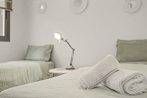 A neatly made bed with a folded towel, a bedside table with a lamp, and two single beds with pillows.