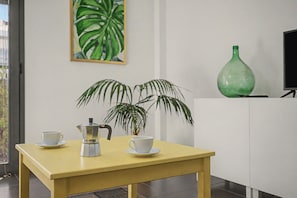 A yellow table with a coffee maker and two cups, a green plant, and a green vase on a white cabinet.