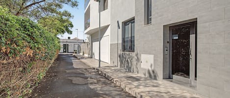 A narrow alleyway with a building on one side, featuring a modern design with large windows and a door with a glass panel.