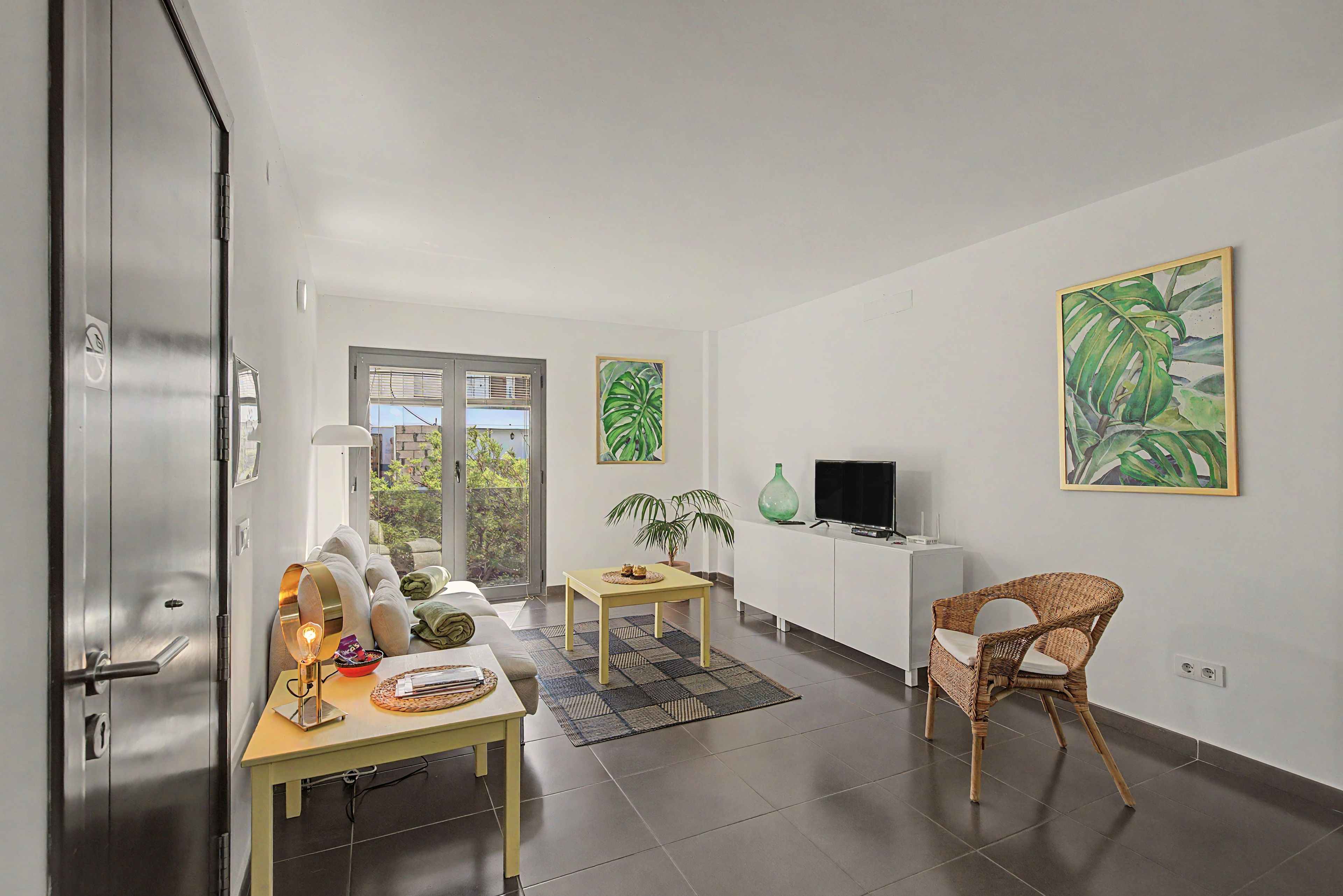 A modern living room with a dining area, a television, and a wicker chair.