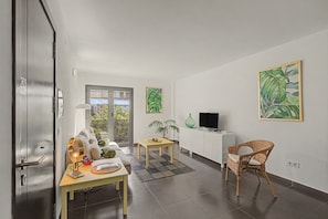A modern living room with a dining area, a television, and a wicker chair.