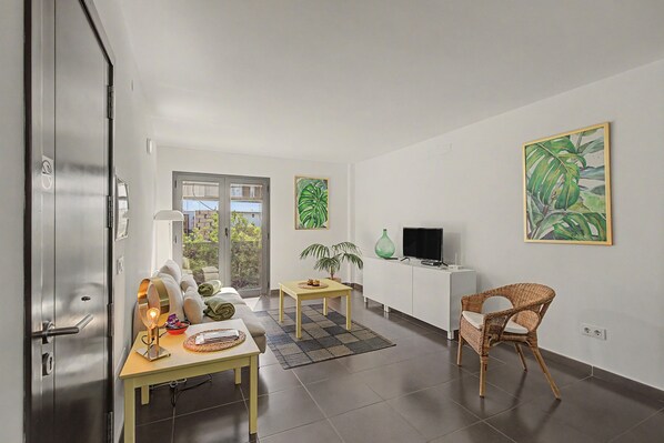 A modern living room with a dining area, a television, and a wicker chair.
